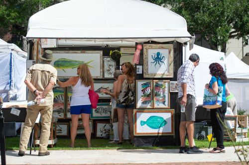 People browsing an art booth featuring marine-themed paintings at an outdoor market.