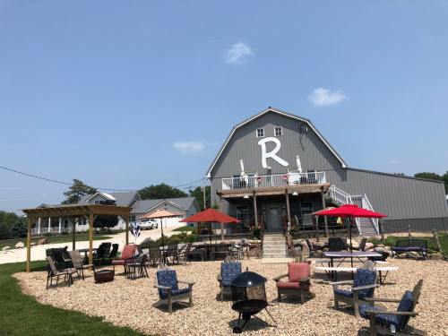 A rustic barn-style building with a large "R" sign, surrounded by outdoor seating and umbrellas on a sunny day.