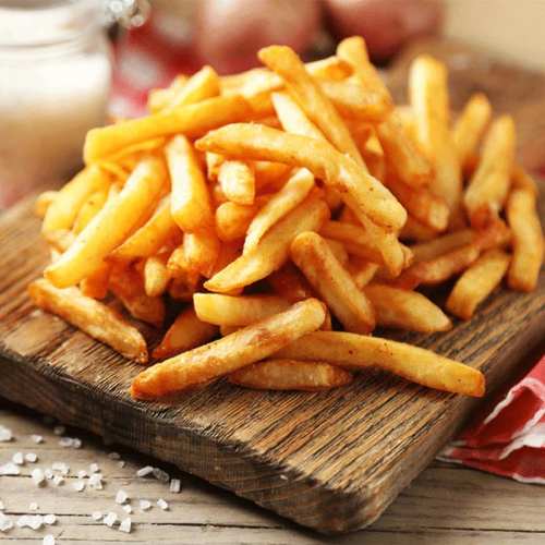 A wooden platter filled with golden, crispy French fries, with a sprinkle of salt and a glass of milk in the background.