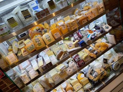 A display case filled with various types of cheese, including blocks, slices, and packaged options.