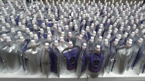 A large number of silver pouches with purple labels and white caps arranged closely together on a surface.