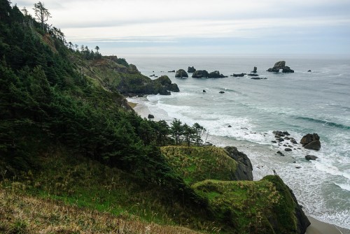 A coastal landscape featuring rocky shores, gentle waves, and lush greenery under a cloudy sky.