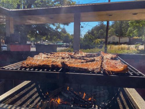 Grilled meat sizzling on a barbecue grill, with smoke rising and a sunny outdoor setting in the background.