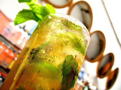 A refreshing cocktail with mint leaves and bubbles, served in a glass, with blurred circular mirrors in the background.