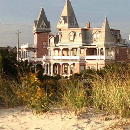 A large, ornate Victorian-style house with multiple spires, surrounded by beach grass and a sandy shore.