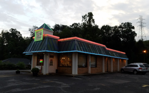 A brightly lit restaurant with a peaked roof and neon accents, surrounded by trees and a parking lot at dusk.