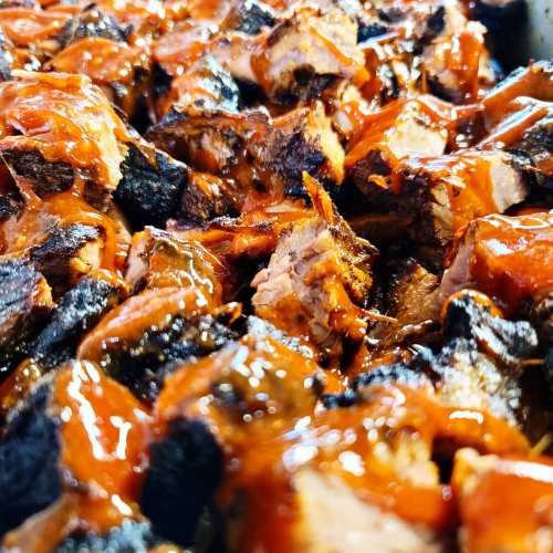 Close-up of tender, smoky barbecue meat coated in a rich, glossy sauce, with charred edges and juicy pieces.