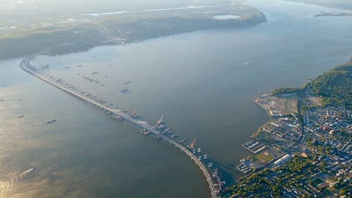 Aerial view of a river with a long pier, boats, and a nearby town along the shoreline.