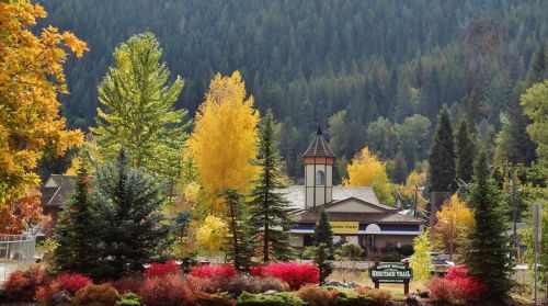A vibrant autumn scene featuring colorful trees and a quaint building nestled in a mountainous landscape.