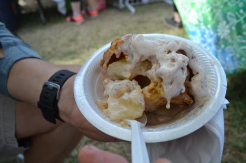 A hand holding a paper plate with a messy dessert topped with cream, featuring chunks of dough and sauce.