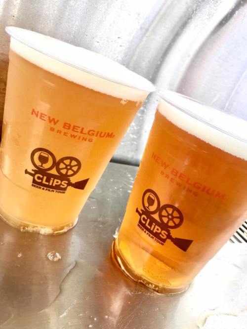 Two plastic cups of light beer with the "New Belgium Brewing" logo, sitting on a metallic surface.