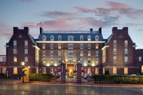 Historic brick hotel with multiple stories, elegant windows, and a flag, set against a colorful sunset sky.