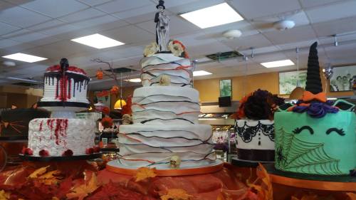 A display of Halloween-themed cakes, including a tiered wedding cake and various decorated cakes with spooky designs.