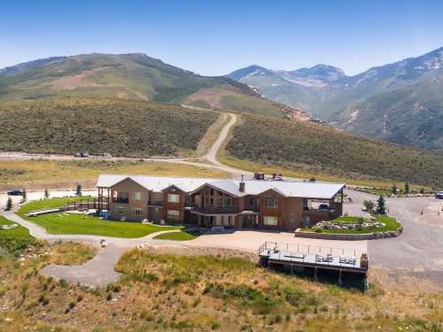 A large, modern building surrounded by green hills and mountains under a clear blue sky.