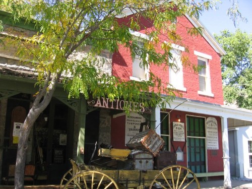 A vintage storefront with a red brick facade, featuring an antique cart and a tree in front.