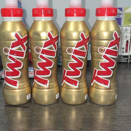 Four gold Twix-branded bottles with red caps, lined up on a wooden surface.