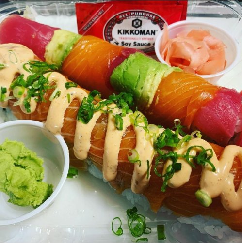 A sushi platter featuring colorful rolls, wasabi, pickled ginger, and soy sauce in a takeout container.