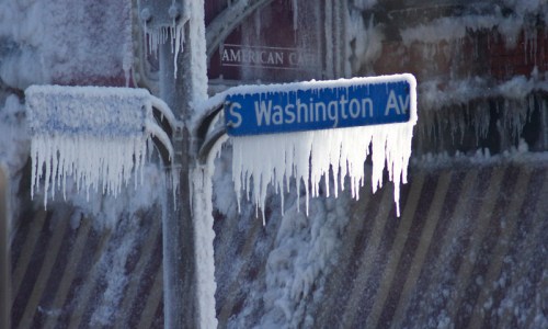 A street sign for S Washington Ave covered in ice and icicles, with a frosty background.