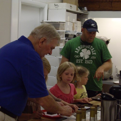 A group of adults and children are engaged in a cooking activity in a kitchen, with various ingredients and utensils around.