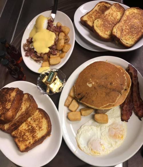 A spread of breakfast items including French toast, pancakes, eggs, bacon, and hash browns, with syrup on the side.