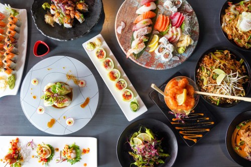 A variety of colorful sushi, sashimi, and Asian dishes beautifully arranged on plates and bowls.