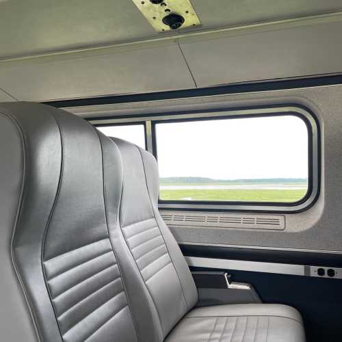 Interior view of a train carriage with two empty gray seats and a window showing a green landscape outside.