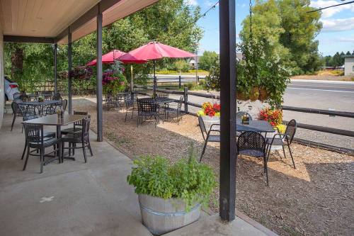 Outdoor seating area with black tables and chairs, red umbrellas, and potted plants along a gravel path.