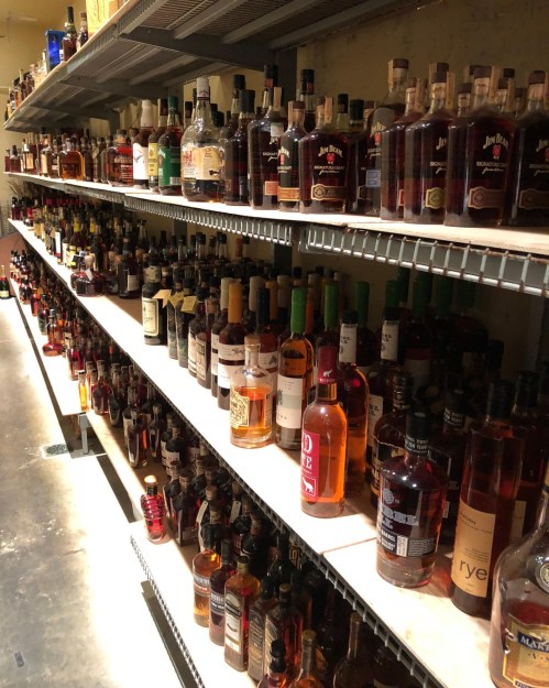 A well-stocked shelf displaying a variety of liquor bottles in a dimly lit storage area.
