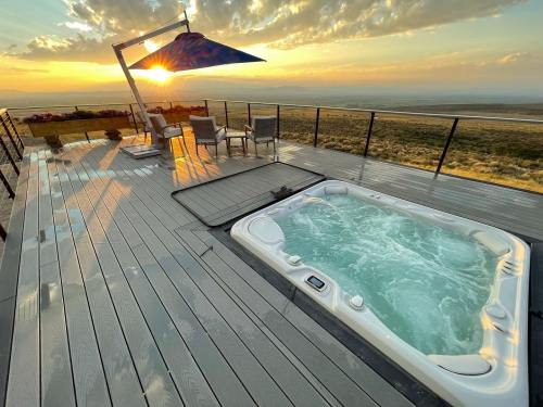 A hot tub on a deck with a sunset view, surrounded by chairs and a colorful shade sail.