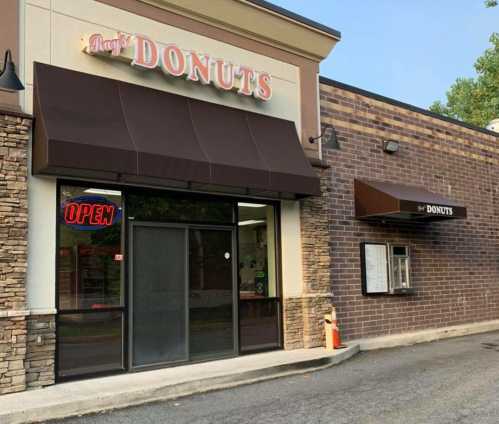 A donut shop with a large "OPEN" sign, featuring a drive-thru window and a brown awning.