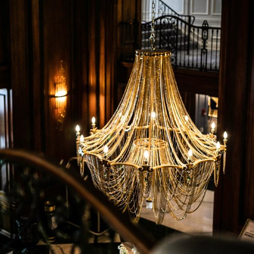 A grand chandelier with cascading beads and multiple lights, hanging in an elegant, wooden interior space.