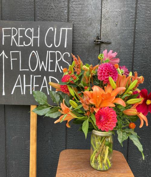 A bouquet of vibrant flowers in a jar next to a sign that reads "Fresh Cut Flowers Ahead."