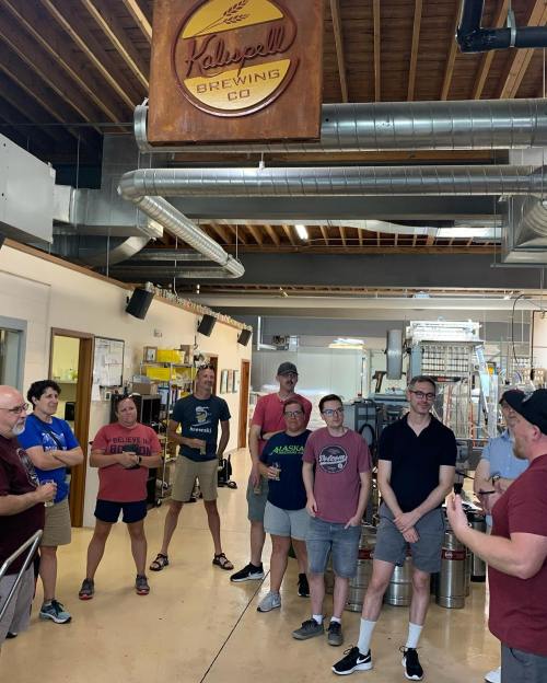 A group of people gathered in a brewery, listening to a speaker near brewing equipment and a sign for Kalleye's Brewing Co.