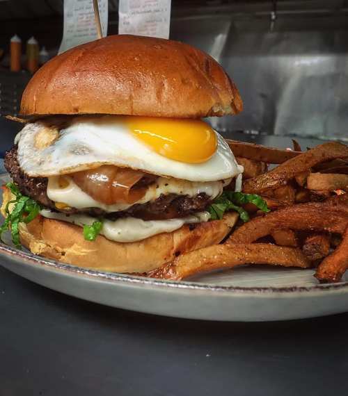 A juicy burger with a fried egg, lettuce, and a toasted bun, served with crispy fries on the side.