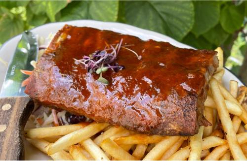 A plate of ribs glazed with sauce, served with crispy fries and garnished with microgreens.