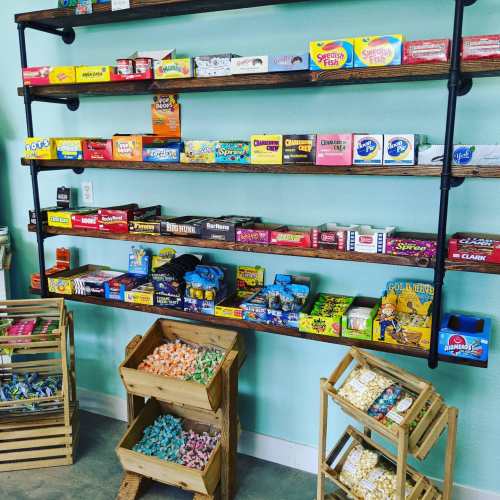 Colorful candy shelves display various treats, with wooden crates filled with sweets in a bright, cheerful shop.