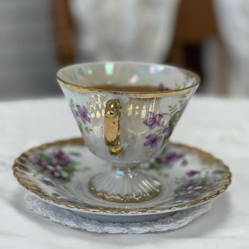 A delicate porcelain teacup with floral designs and a gold rim, resting on a matching saucer.