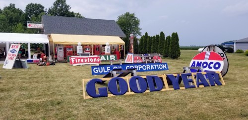 Vintage gas station display with signs for Firestone, Gulf Oil, Amoco, and Goodyear, set in a grassy area.