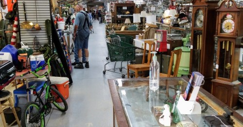 A bustling antique store aisle filled with various items, including furniture, bicycles, and vintage decor.
