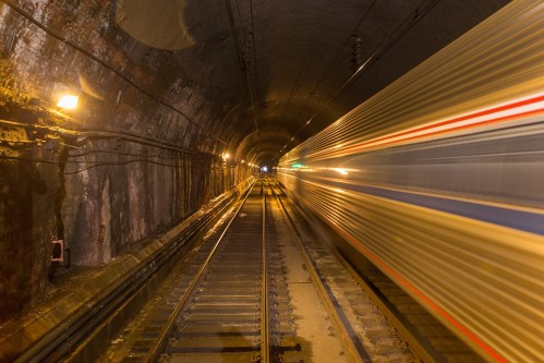 A train speeds through a dimly lit tunnel, with blurred motion and illuminated tracks on either side.