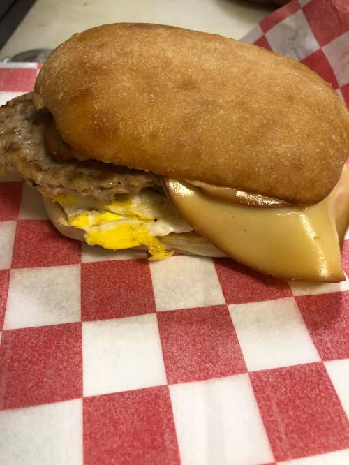 A breakfast sandwich with sausage, egg, and cheese on a soft bun, served on red and white checkered paper.