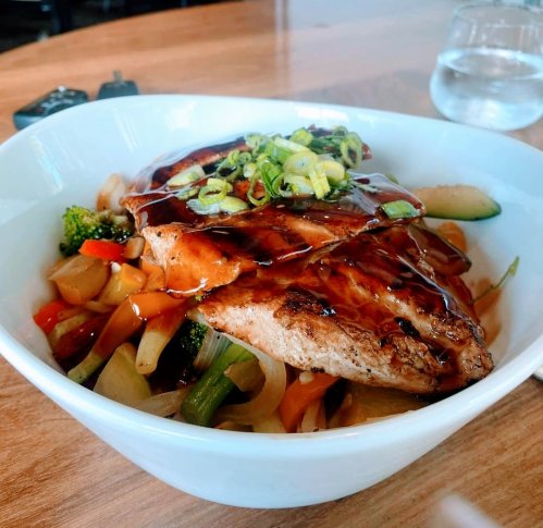 A bowl of grilled chicken topped with green onions, served over a colorful mix of sautéed vegetables.
