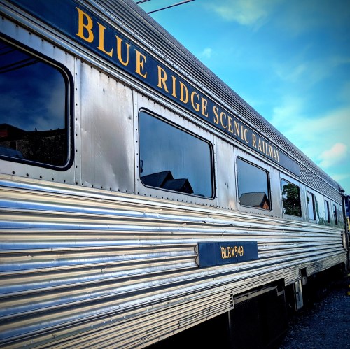 A silver train car with "Blue Ridge Scenic Railway" written on the side, set against a blue sky.