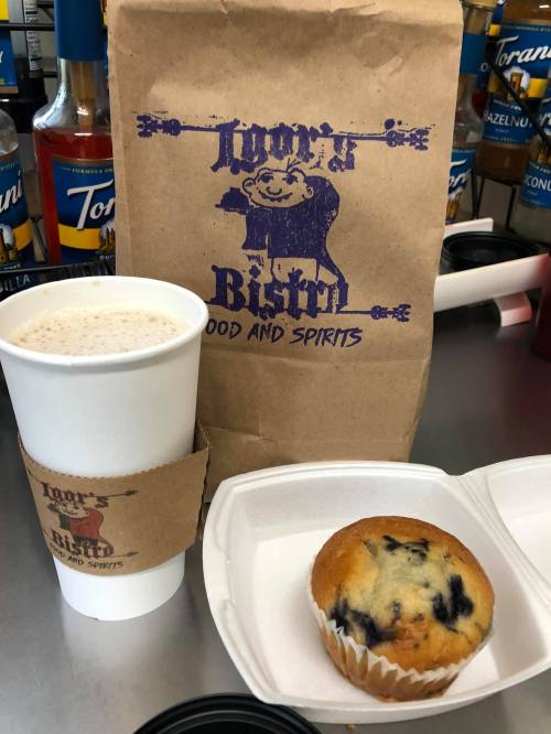 A takeout bag from Door's Bistro, a coffee cup, and a blueberry muffin on a counter.