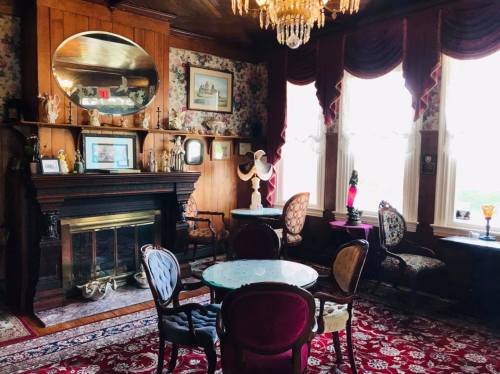 A vintage parlor with ornate furniture, a fireplace, and floral wallpaper, featuring a chandelier and decorative accents.