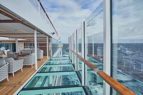A modern cruise ship deck with glass railings overlooking the ocean, featuring stylish seating areas.