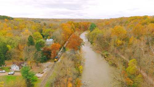 Aerial view of a river winding through autumn-colored trees, with a train track and a house nearby.