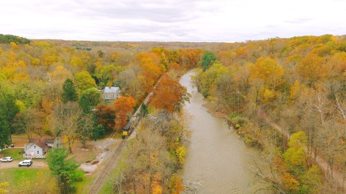 Aerial view of a river winding through autumn-colored trees, with a train track and a house nearby.