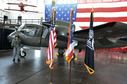 A military aircraft displayed indoors with flags and a mannequin in a pilot's uniform standing nearby.