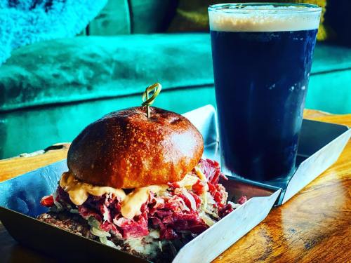A close-up of a hearty sandwich with pulled meat and sauce, served with a dark beer in a glass on a wooden table.